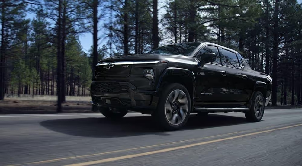 Black 2024 Chevy Silverado EV is driving on a tree-lined road
