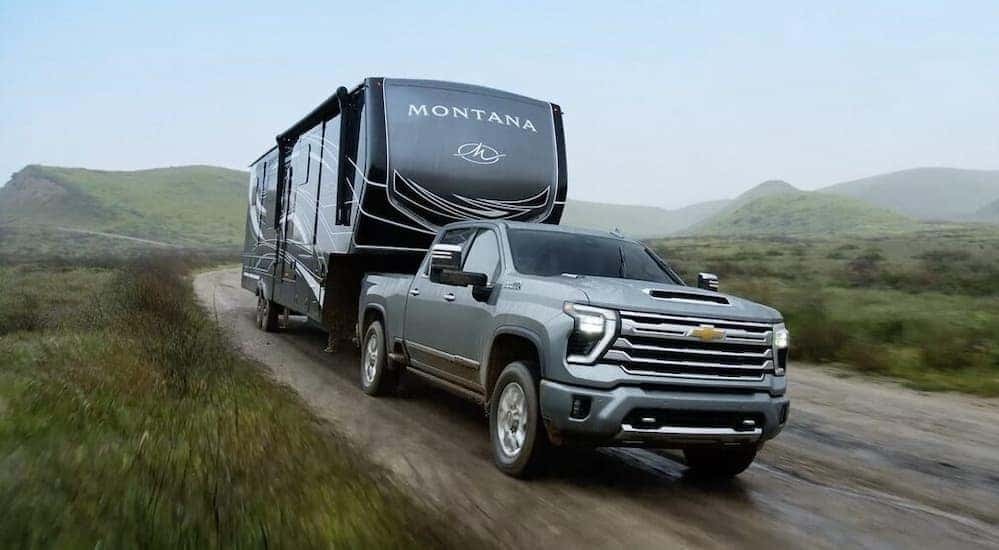 A gray 2024 Chevy Silverado 2500 HD High Country is shown towing a trailer to view trucks for sale