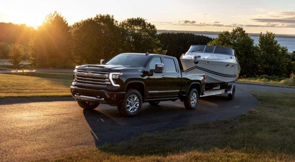A black 2024 Chevy Silverado 2500 HD High Country is shown towing a boat.