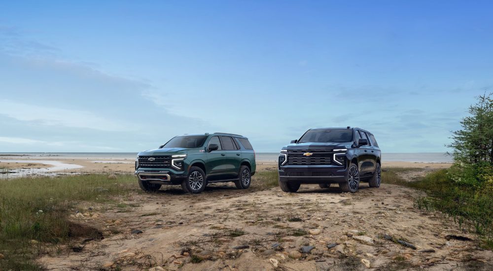 Green 2025 Chevy Tahoe Z71 and a blue Suburban High Country parked off-road