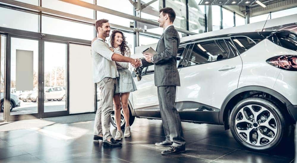 A couple are shown speaking to a car salesman at a dealership after searching "sell my car."