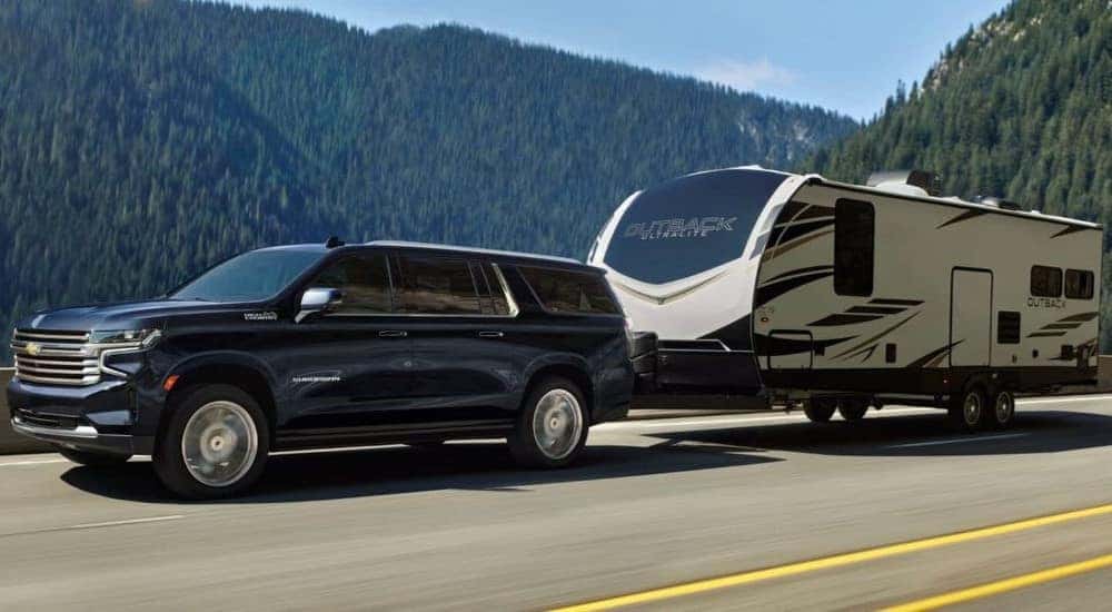 A popular used Chevy Suburban for sale, a black 2023 Chevy Suburban High Country, is shown towing a trailer.