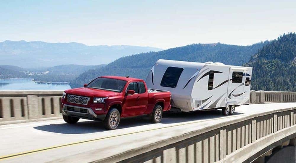A red 2023 Nissan Frontier towing a trailer over a bridge.