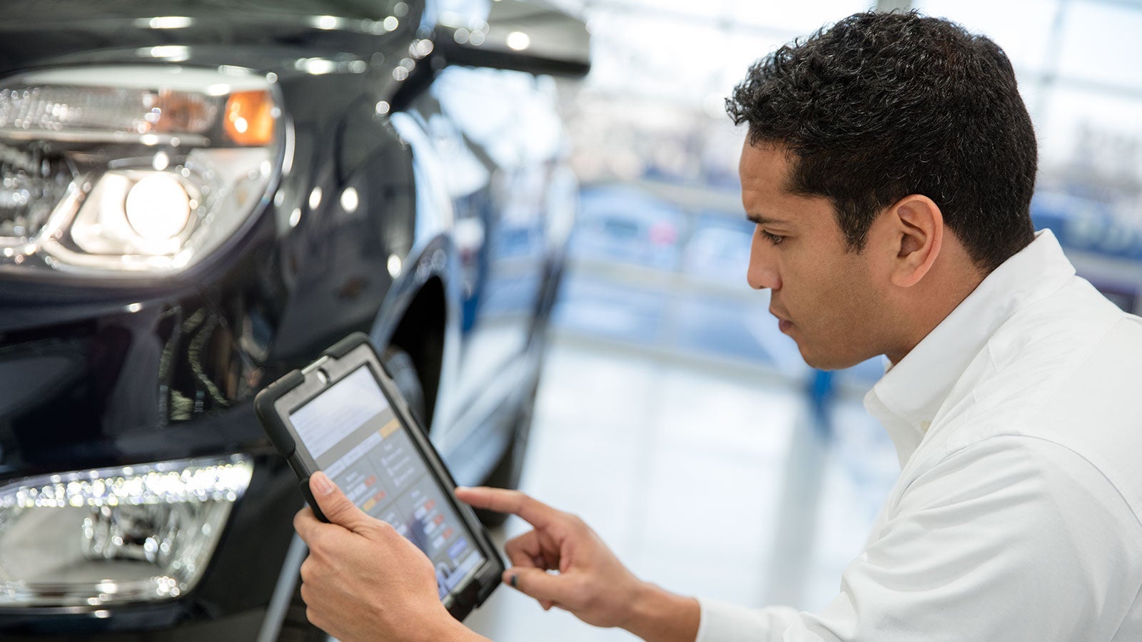 A service technician using a tablet while inspecting a vehicle