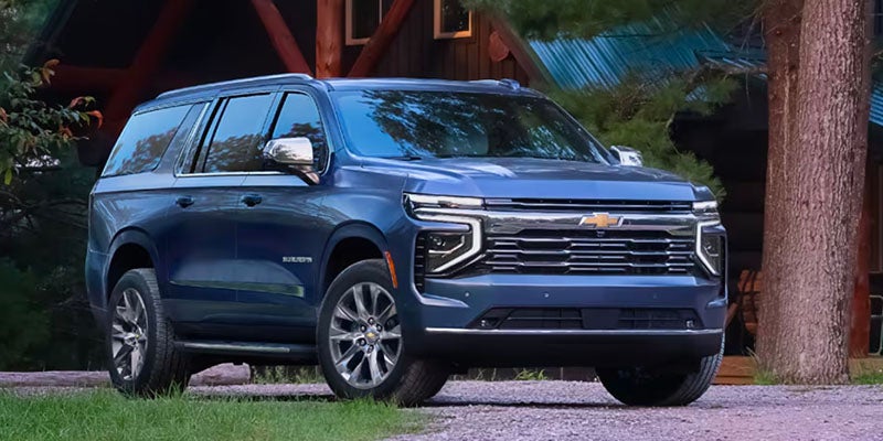 A blue Chevrolet Suburban parked in front of a rustic log cabin.