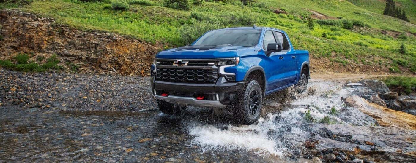 A blue 2023 Chevy Silverado 1500 ZR2 driving through a creek.