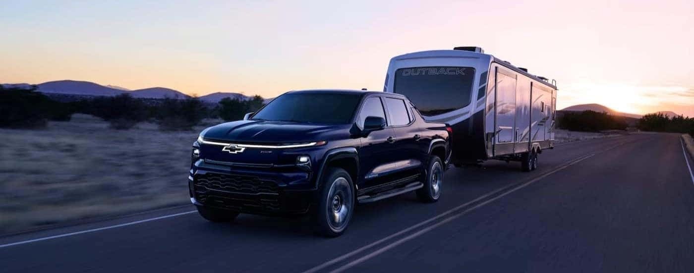 A black 2025 Chevy Silverado EV RST is shown towing a trailer on a highway.