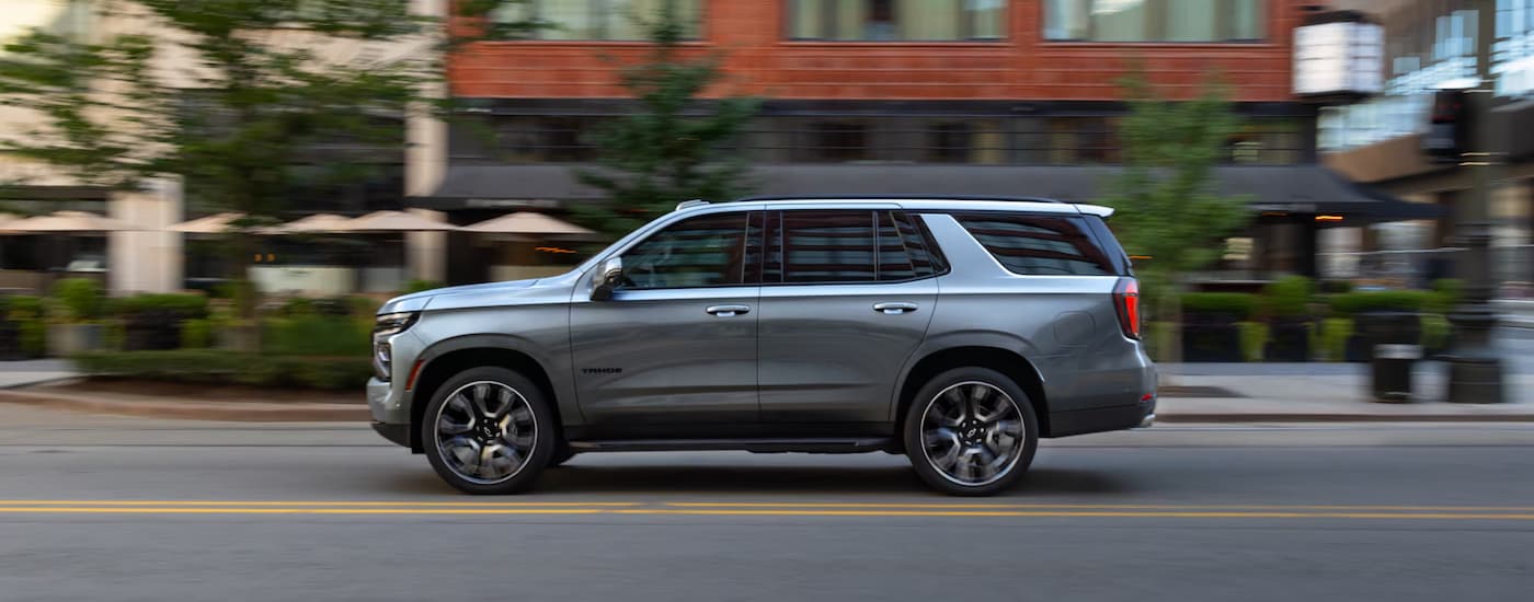 Side of a silver 2026 Chevy Tahoe driving down a city street.