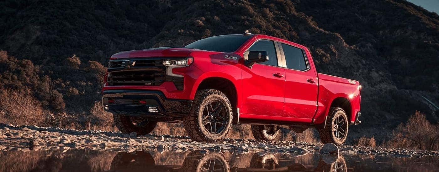 A red 2023 Chevy Silverado 1500 Z71 is shown parked on rocked next to a small pond."