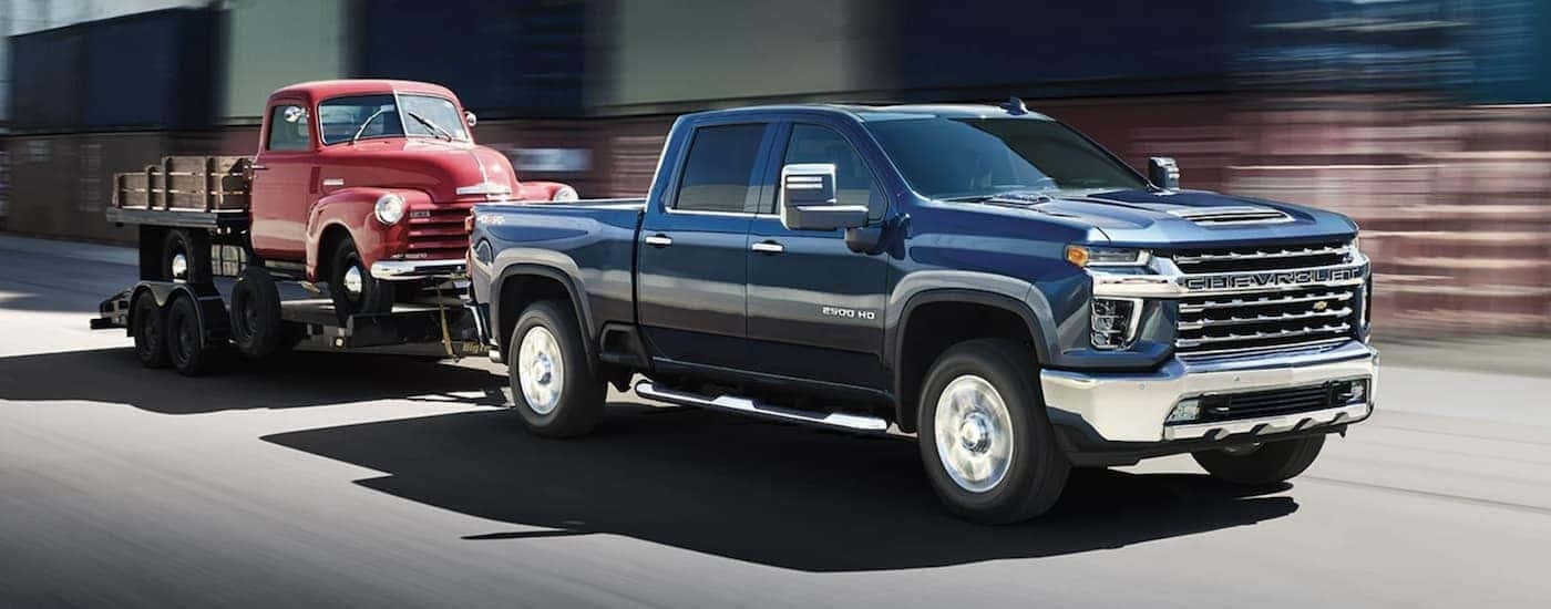 A blue 2023 Chevy Silverado 3500 HD is shown towing a vintage truck.