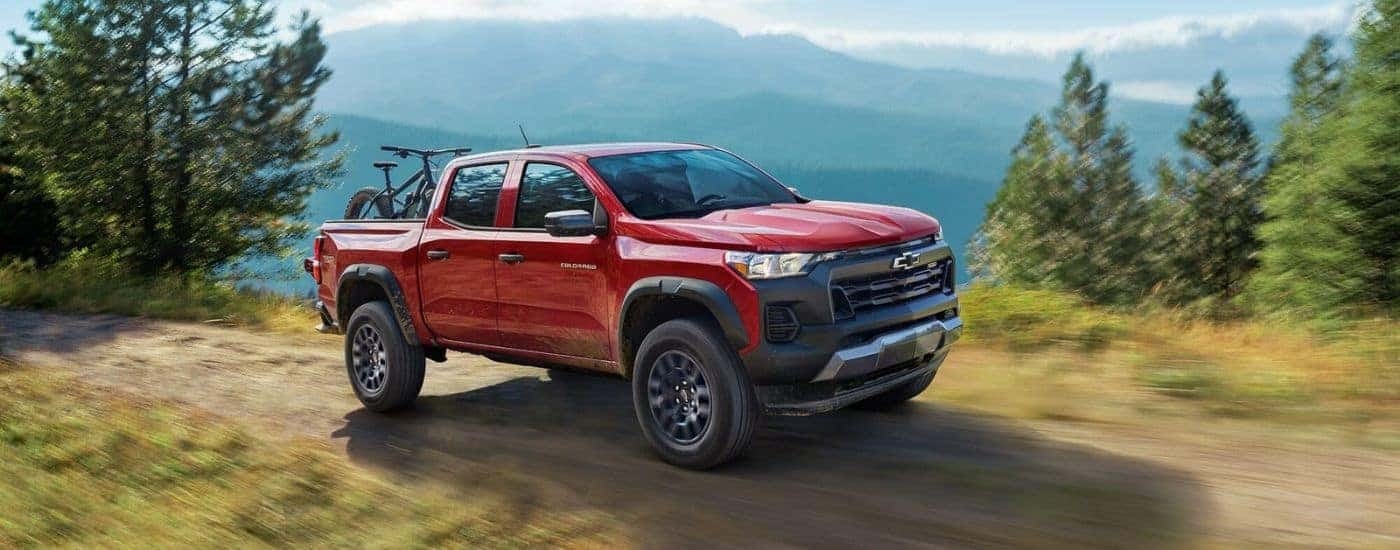 A red 2023 Chevy Colorado is shown driving near a mountain after viewing trucks for sale.
