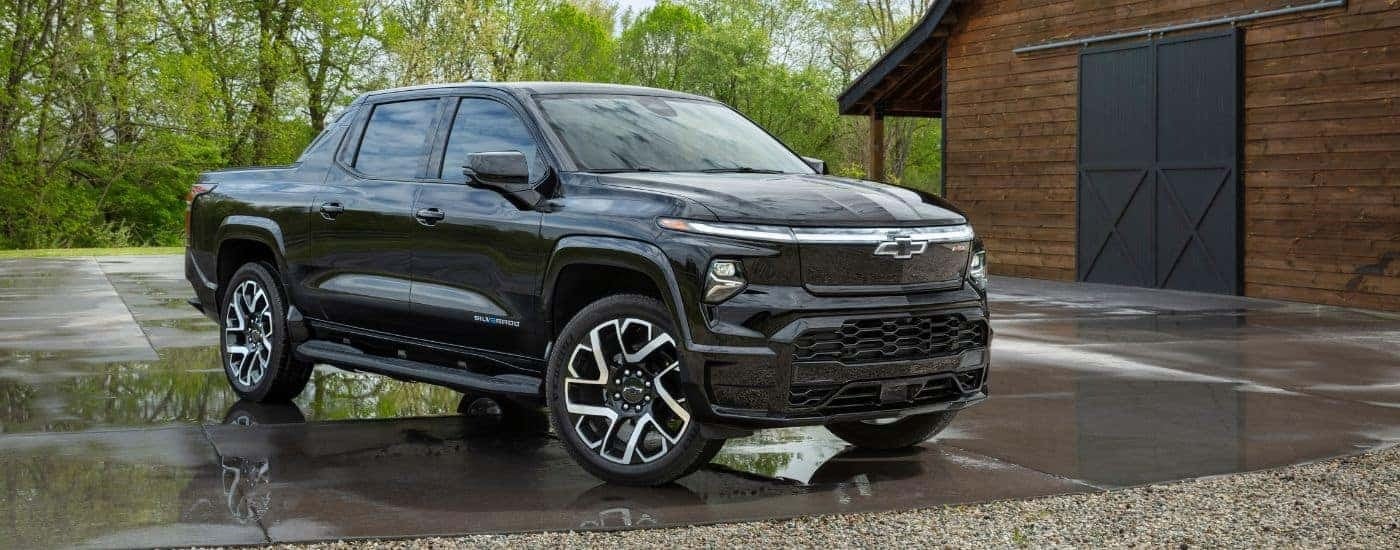 A black 2024 Chevy Silverado EV RST is shown parked in front of a barn
