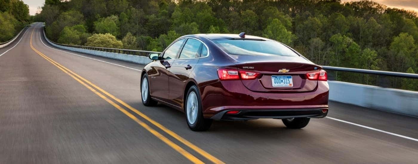 A purple 2018 Chevy Malibu is shown from the rear driving on a cloudy day.