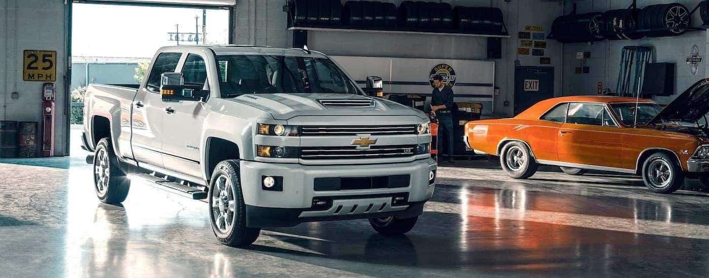 A white 2017 Chevy Silverado 2500HD LTZ is shown parked in a garage next to a muscle car.