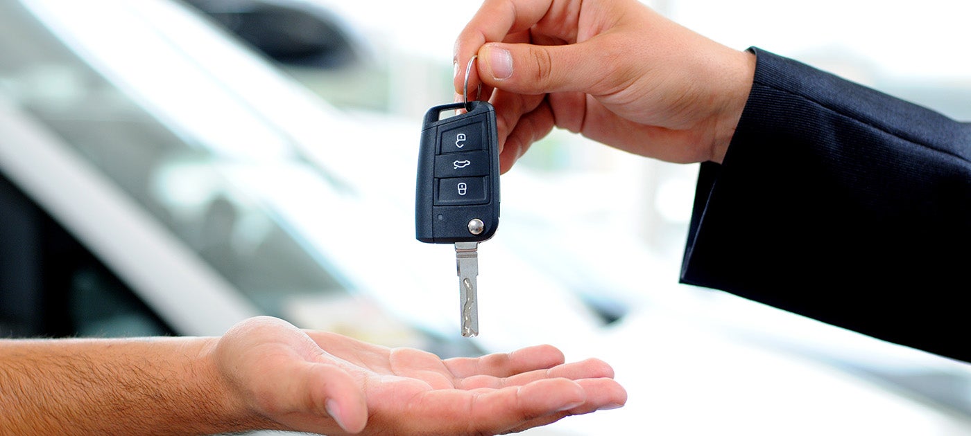 A hand in a suit drops a car key into an open palm