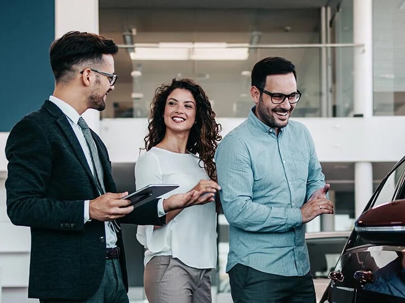Smiling couple looking at a new car with a dealership salesman